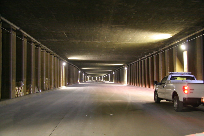 A white pickup truck is parked inside a wide, well-lit underground tunnel with concrete columns along the sides.