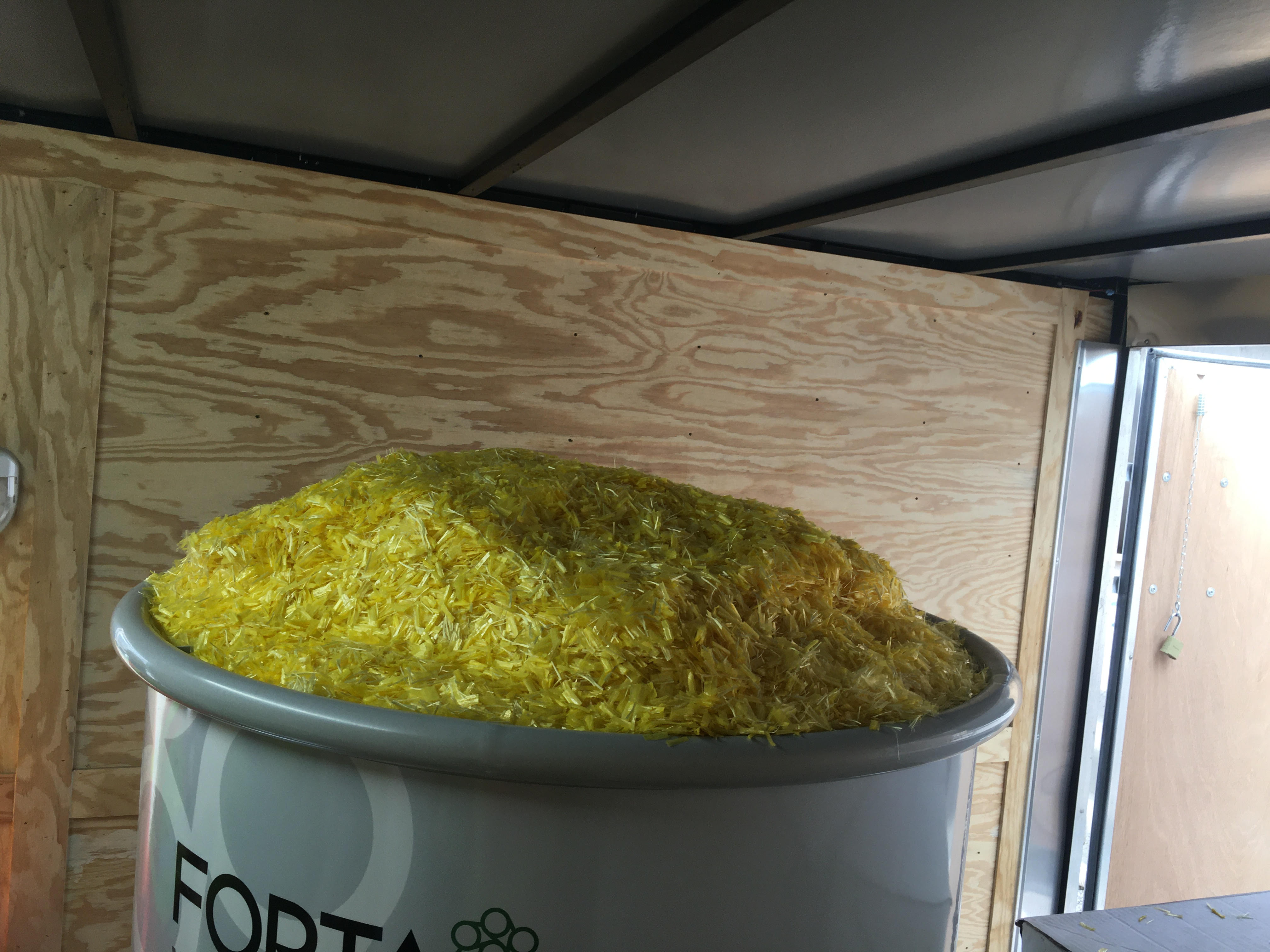 A large container filled to the top with yellow shredded material sits in a wooden-paneled room.