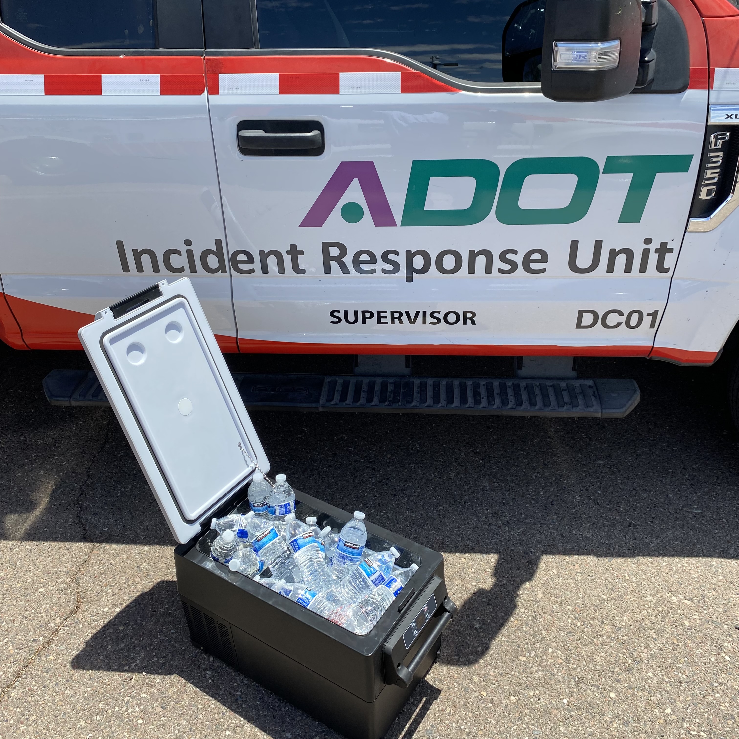 Cooler with water bottles in front of an ADOT Incident Response Unit truck on a sunny day.