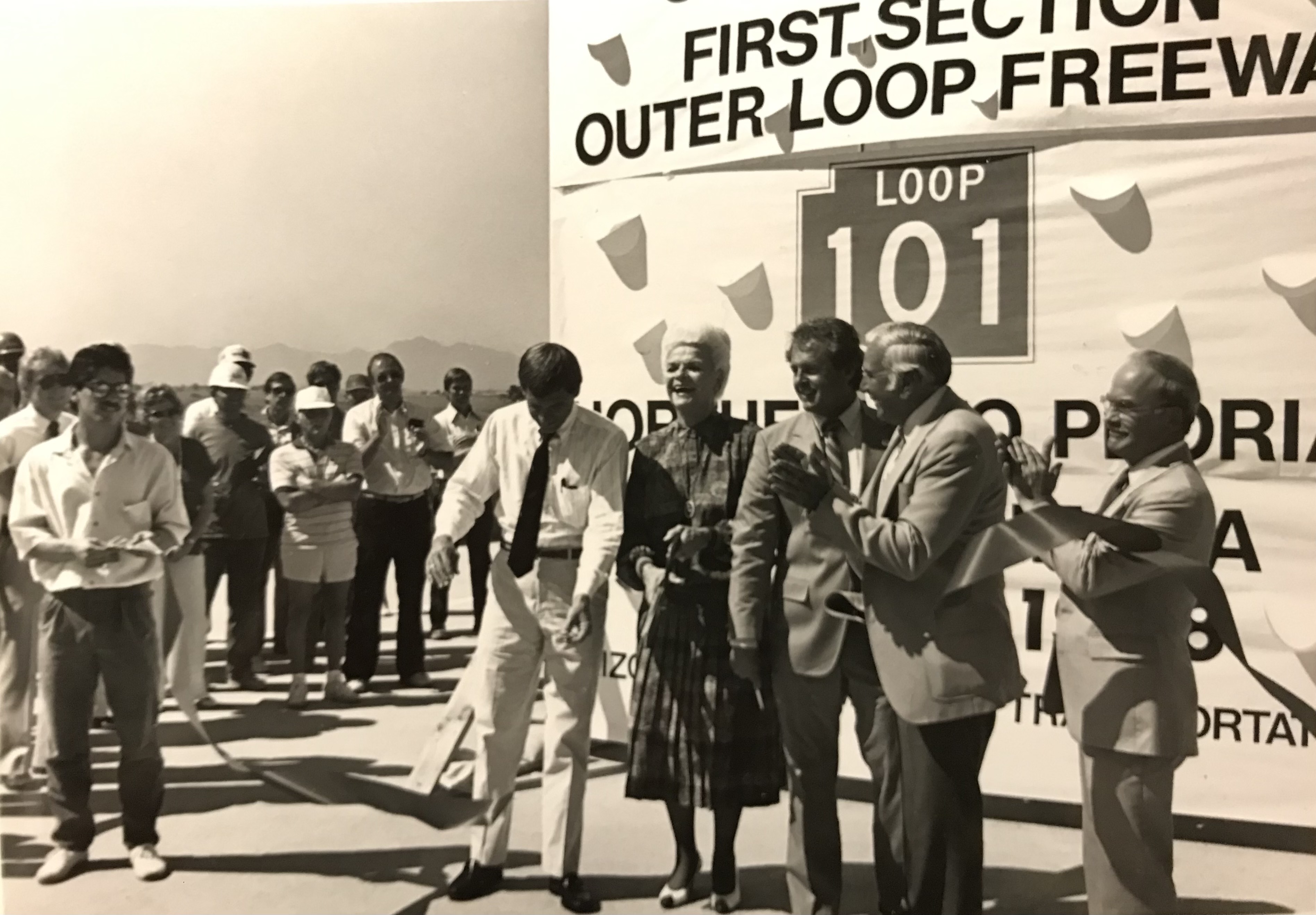 Black and white image of people in front of large Loop 101 grand opening sign