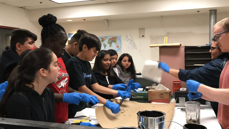 Students watch ADOT workers test materials on a table.