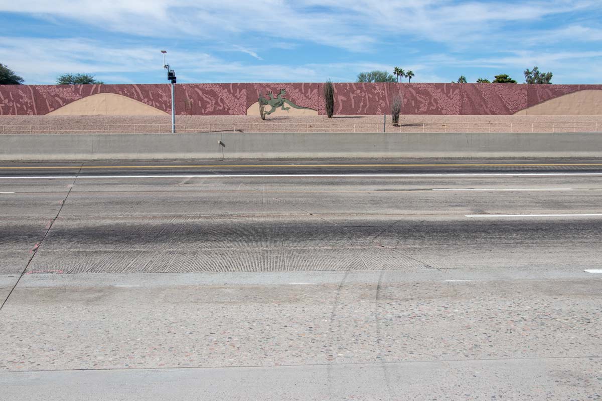 View of Loop 101 freeway lanes with decorative sound wall featuring desert-themed artwork during improvement construction.