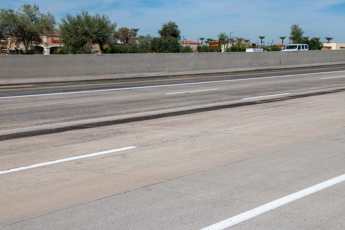 Loop 101 freeway lanes with visible pavement wear and adjacent shopping center in background during road improvement work.