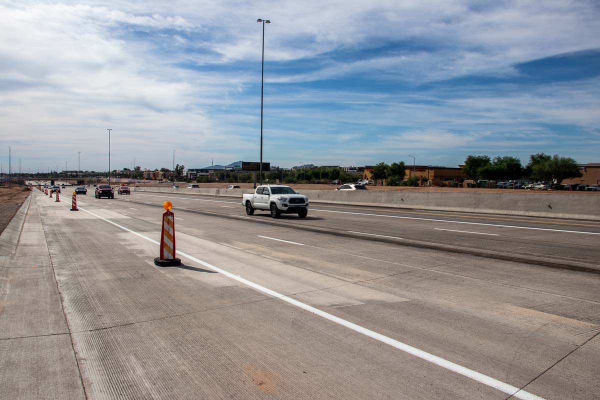 Construction barrels and traffic on newly paved Loop 101 freeway lanes during improvement activities.