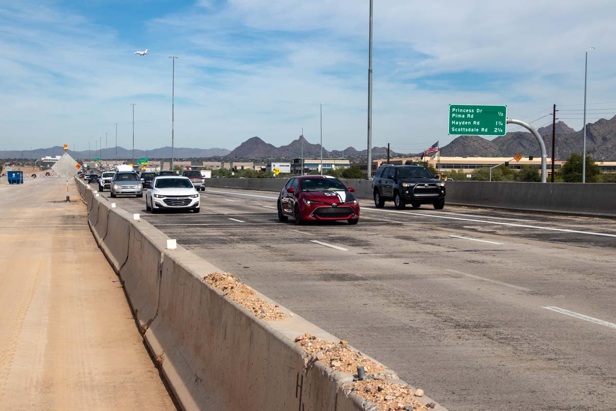 Loop 101 northbound lanes with construction barriers and roadwork materials, mountains visible in the distance.