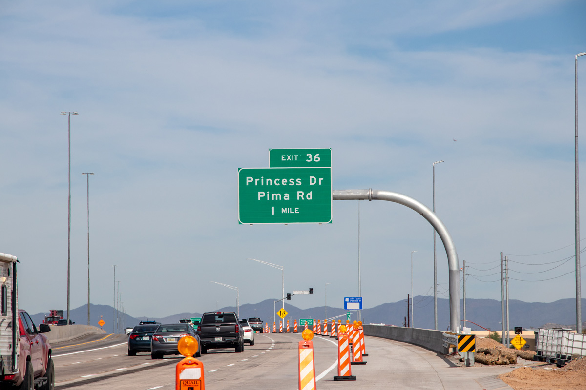 Wide view of freshly milled Loop 101 freeway lanes with sound walls and traffic in the distance under a clear sky.