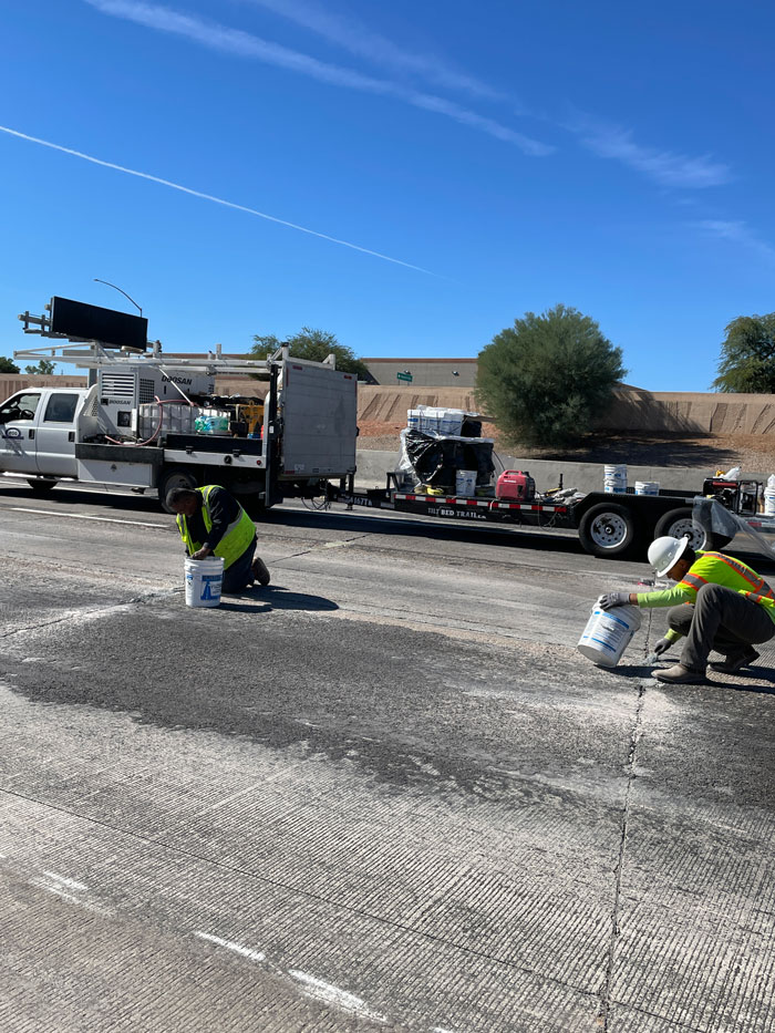 Crews performing pavement crack sealing on Loop 101 with work vehicles parked along the shoulder.
