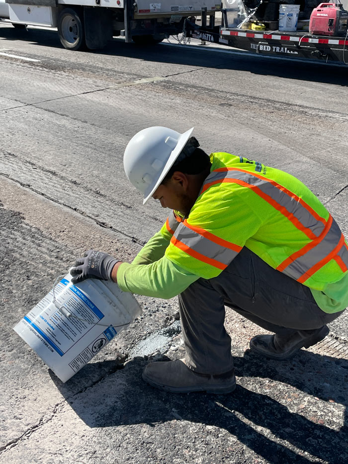 Worker smoothing crack-seal material into a pavement joint on Loop 101 during maintenance operations.