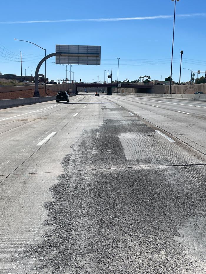 Freshly milled Loop 101 freeway pavement leading toward an overpass with light traffic and clear skies.