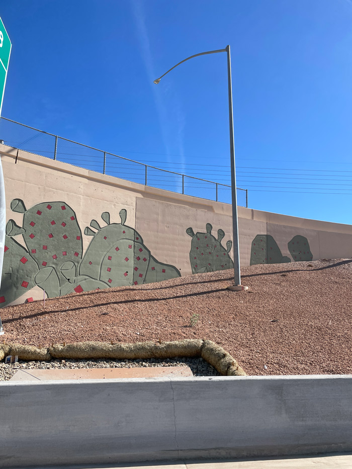 Road construction vehicles and arrow board sign staged on Loop 101 near a lane merge warning sign.