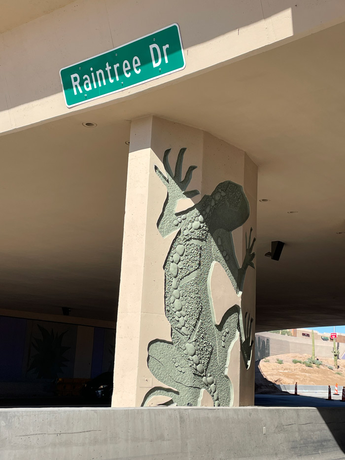 Decorative gecko artwork on a bridge pillar at a Loop 101 underpass with vehicles traveling beneath..