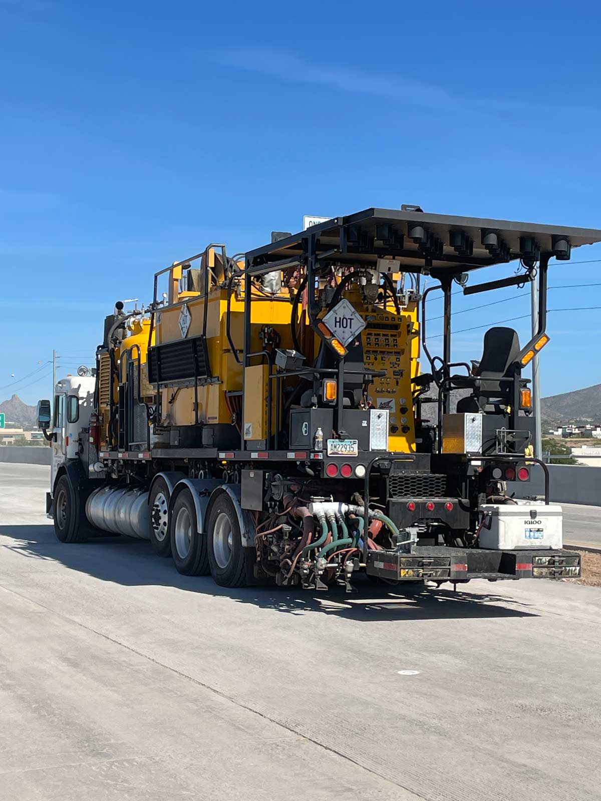 Yellow road maintenance truck with equipment parked on freshly paved Loop 101 lanes during construction work.