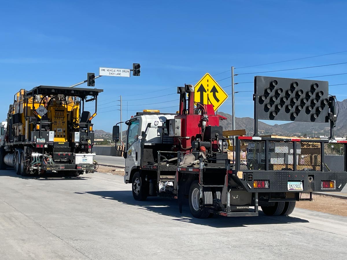 Road construction vehicles and arrow board sign staged on Loop 101 near a lane merge warning sign.
