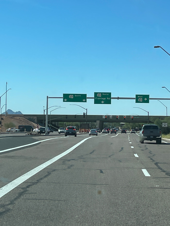 Traffic approaching the Loop 101 southbound and Frontage Road on-ramps, with overhead guide signs and an overpass in the background.