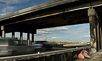 Cars driving quickly under a highway overpass, with fields in the background.