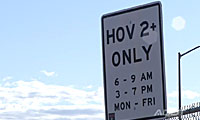 A road sign reads HOV 2+ ONLY, 6-9 AM, 3-7 PM, MON-FRI against a partly cloudy sky.