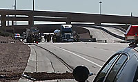 Police vehicles and a semi-truck block a highway on-ramp under an overpass, with officers and emergency personnel standing nearby.
