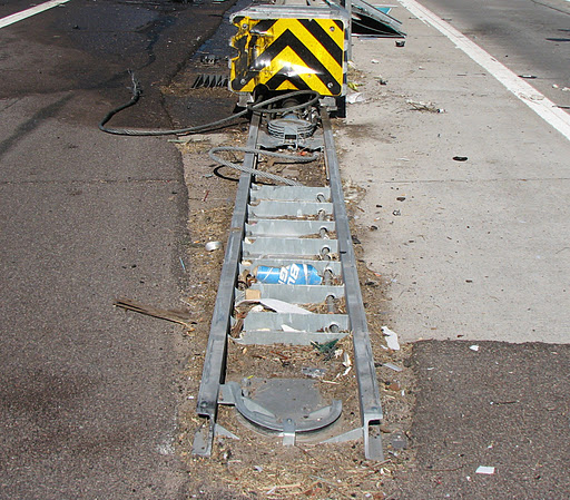 Damaged crash barrier with black and yellow stripes on a roadside, metal parts bent and debris scattered.