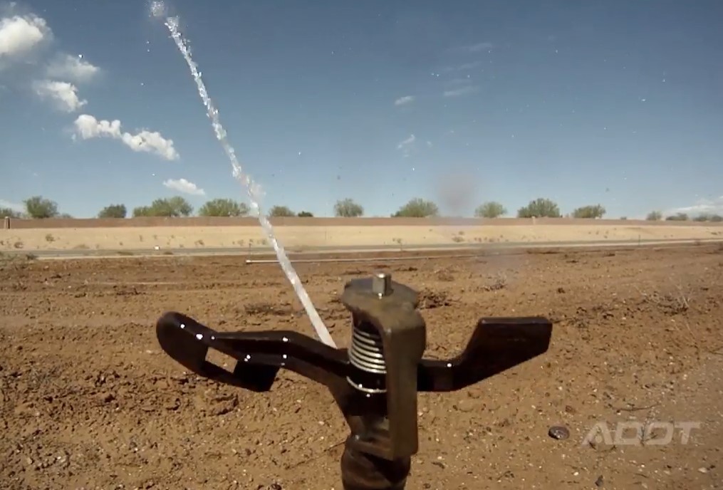 Sprinkler wets earth at highway construction site. 