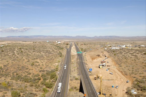 A highway stretches through a dry landscape with cars and construction equipment on the roadside.