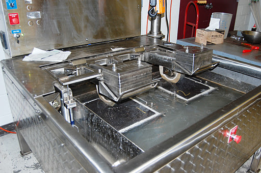 A large industrial machine with metal trays and rollers used for testing asphalt and other road materials.