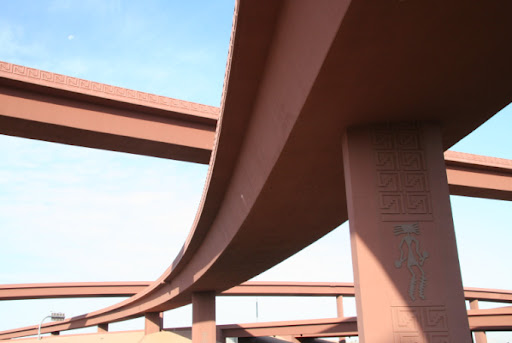 Brown freeway overpasses with geometric patterns against a blue sky, viewed from below.