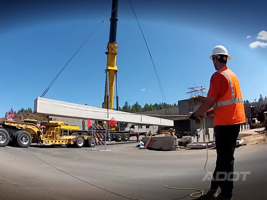 Crane lifts box girder from truck trailer.
