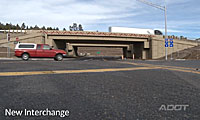 Red SUV and white truck drive near a new highway interchange under an overpass, with road signs visible.