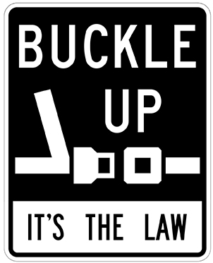 Black and white sign showing a seatbelt icon with the words “Buckle Up, It’s the Law.”.