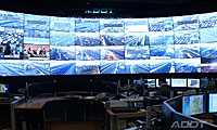 A control room with many monitors displaying live traffic camera feeds on a large curved wall screen.