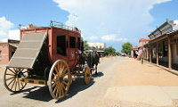 A horse-drawn stagecoach travels down a deserted, sunlit street in the historic town of Tombstone Arizona with wooden buildings on either side.