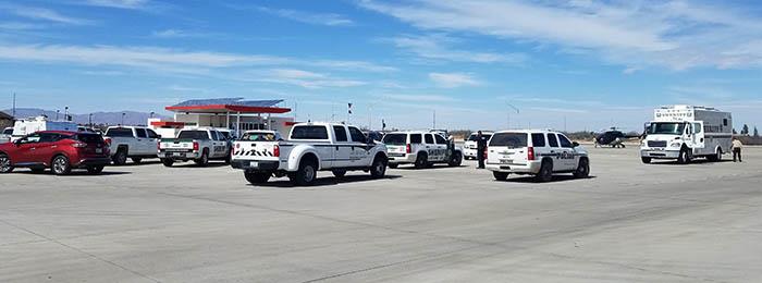 Multiple emergency response vehicles are parked in a large open lot under a blue sky with scattered clouds.