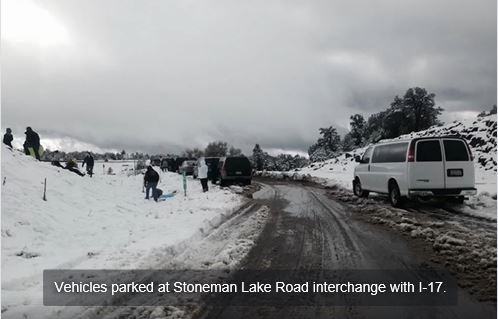 Several vehicles are parked at the Stoneman Lake Road interchange with I-17 and people are standing around in the snow at the roadside.