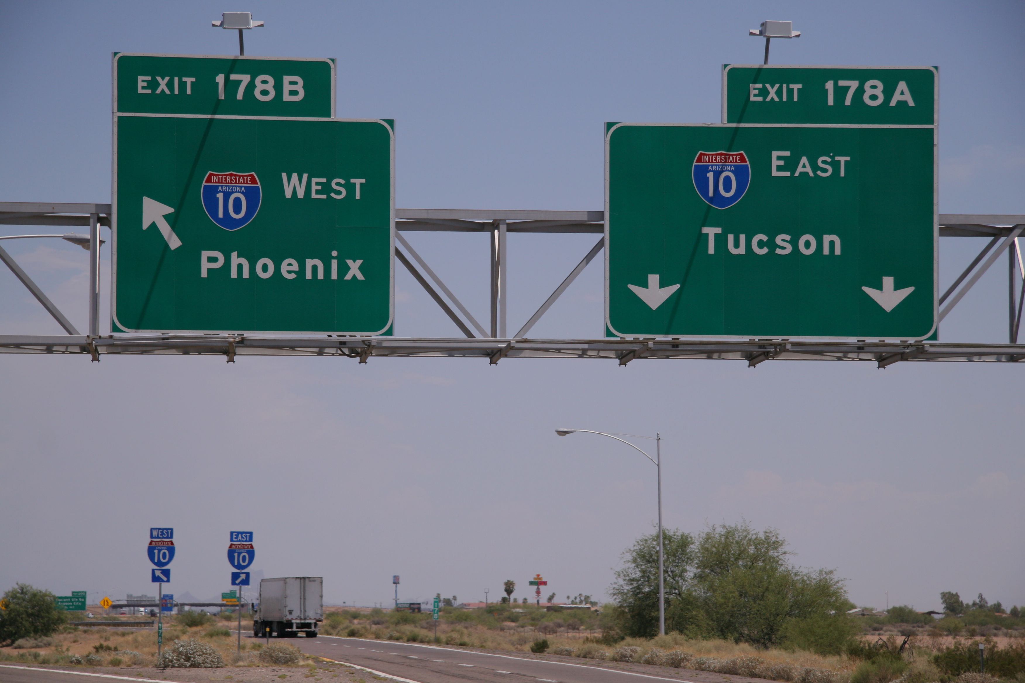 Overhead highway signs show directions for I-10 West to Phoenix (Exit 178B) and I-10 East to Tucson (Exit 178A) above a road with a truck driving.