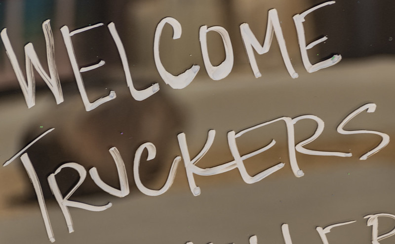 White handwritten text on a window or glass says WELCOME TRUCKERS with a blurred indoor background visible behind the writing.
