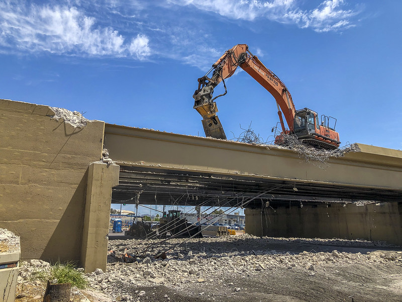 An excavator demolishes the top of a concrete bridge.