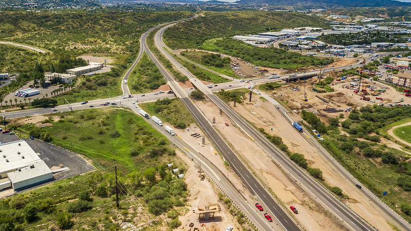 Aerial view of a highway intersection with surrounding greenery and some buildings under a partly cloudy sky.