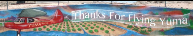 A mural shows a red airplane flying over fields and a river with a banner that reads, Thanks for Flying Yuma.