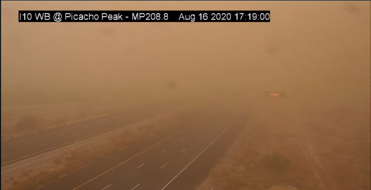 A highway near Picacho Peak is barely visible due to thick dust from a sandstorm, with very low visibility and a faint traffic sign in the background.