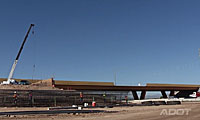 A crane and construction equipment are positioned near an unfinished highway overpass under a clear blue sky.