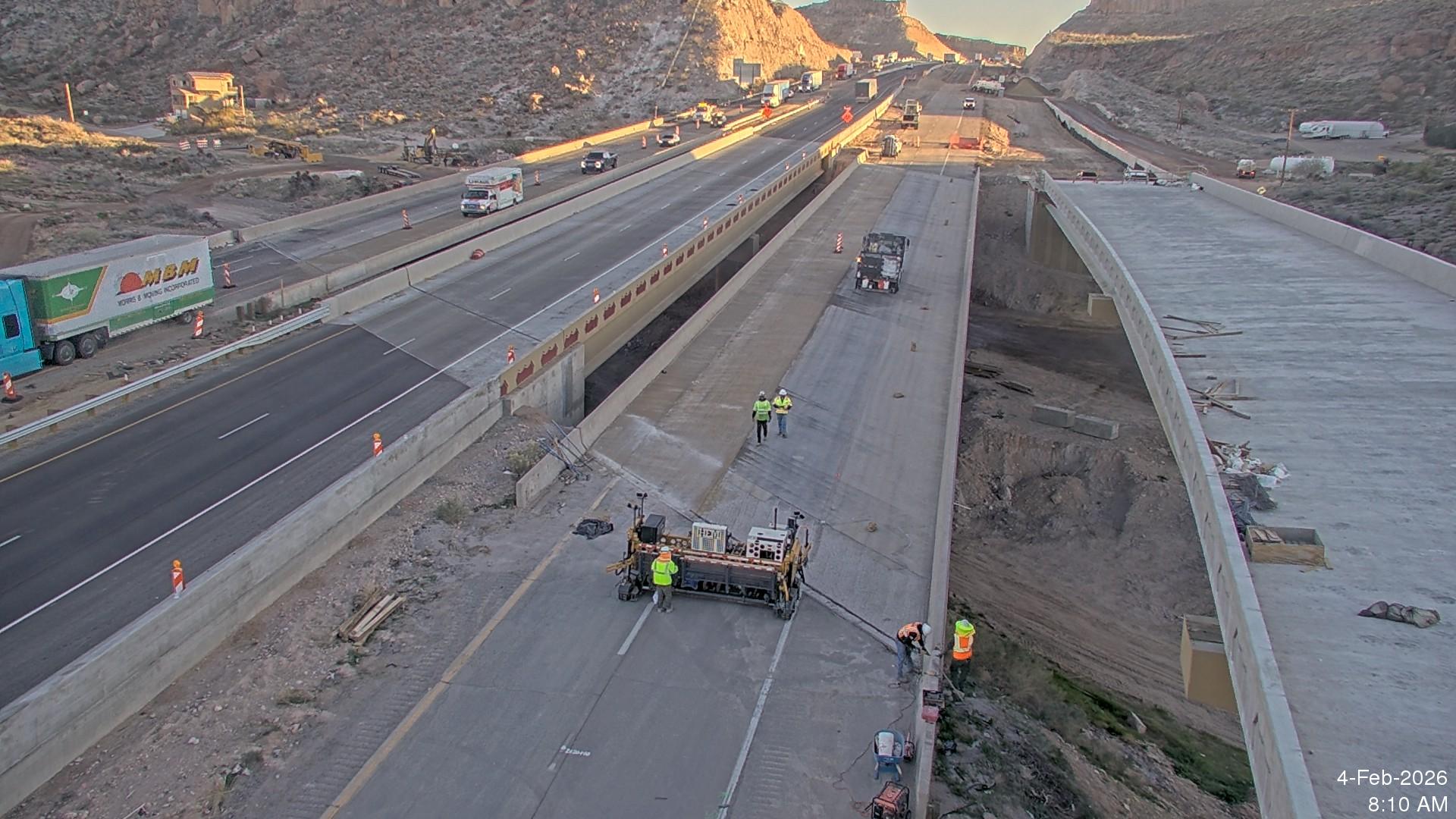 Aerial view of construction crews working on a new elevated roadway segment connecting I-40 and US 93 in Kingman, with active interstate traffic and bridge structures under development in a desert canyon setting.