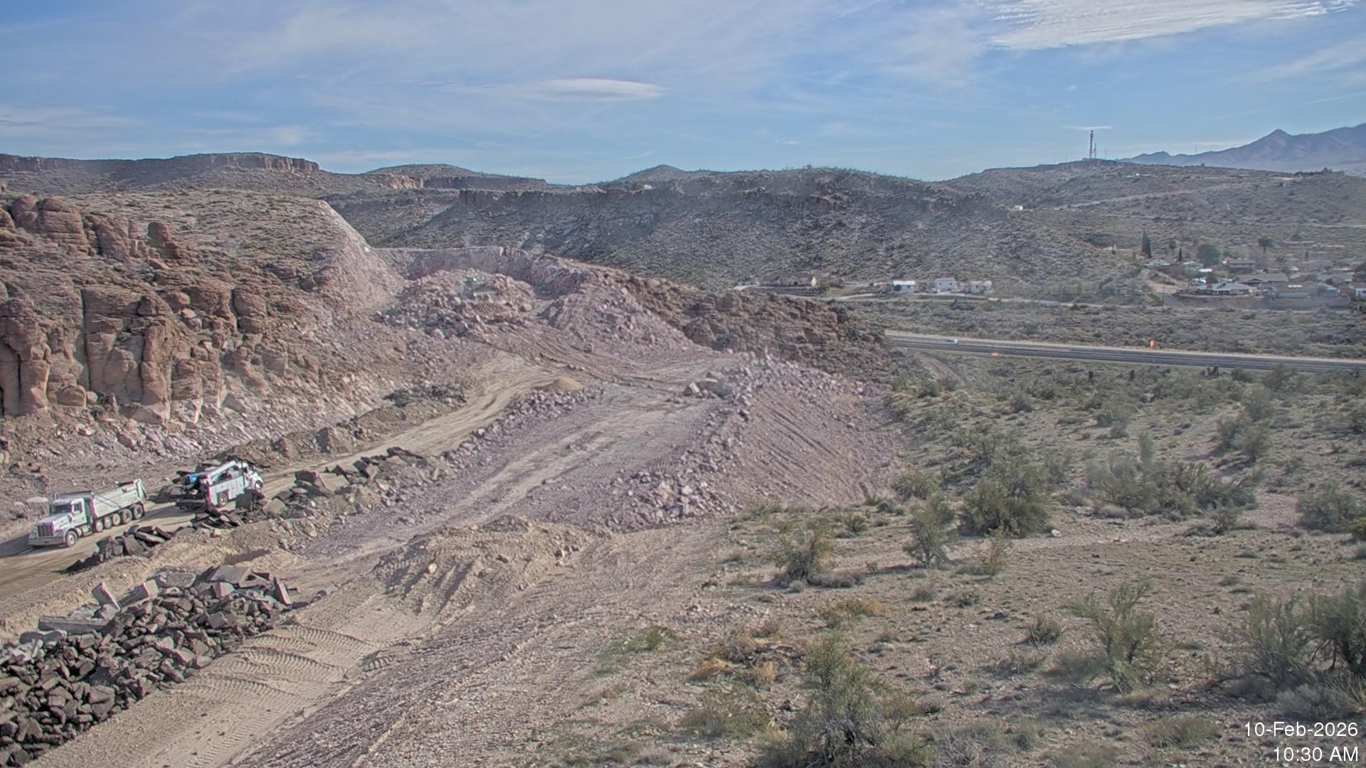 Rock excavation and grading work for the new US 93 alignment near I-40 in Kingman, with haul trucks and heavy equipment operating in a desert canyon landscape adjacent to the interstate.