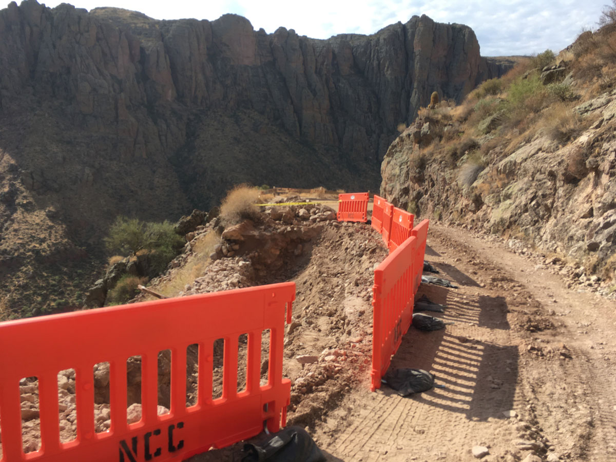 Temporary orange safety barriers installed along the edge of a damaged mountain roadway.