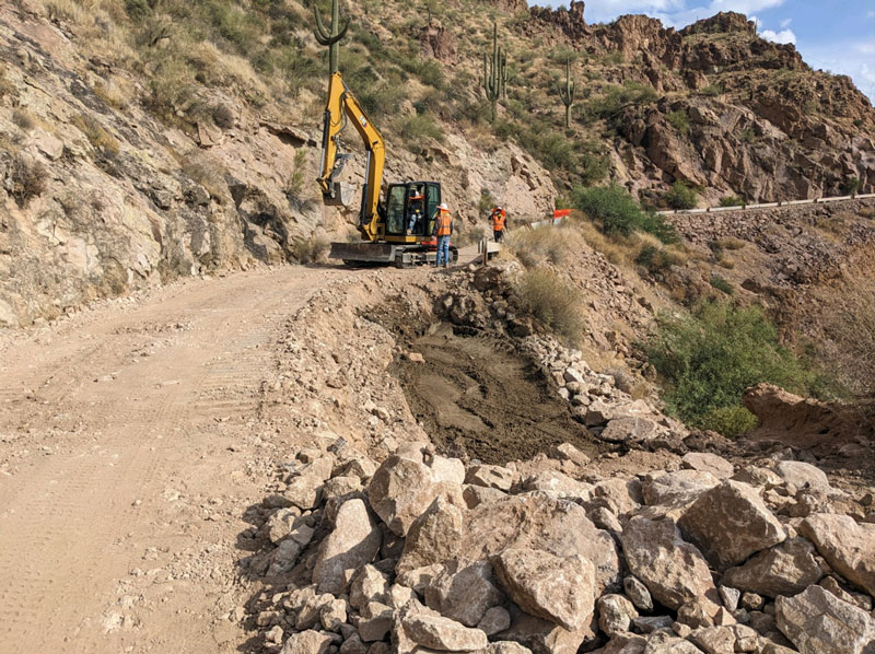 Construction crew in safety vests reviewing canyon roadway repair progress on SR 88.