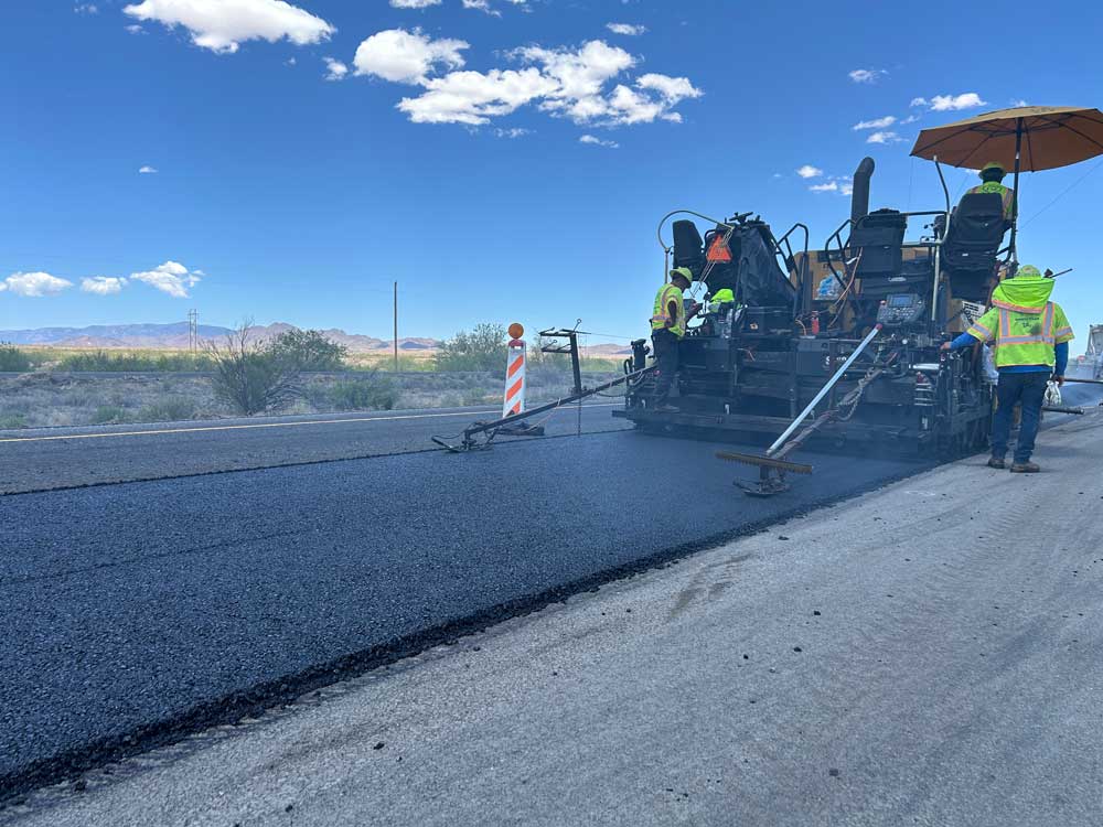 Highway workers operate an asphalt paver while resurfacing Interstate 10