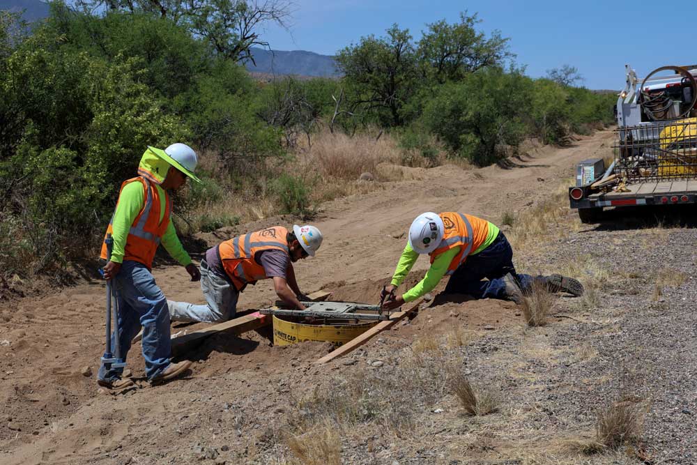 three construction crew members working on the roadside with heavy machinery