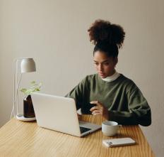 A woman sits at a table, working on a computer.