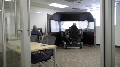 Man operating a snowplow simulator while another observes his progress