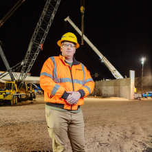 A man in an orange reflective gear stands in a construction area.