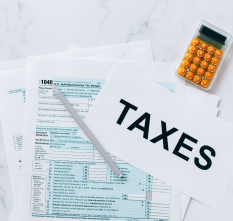 A calculator and a tax form with a pen on top. Also a sign with the word "Taxes" written on it.